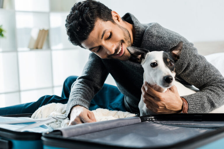 gut aussehender und lächelnder gemischtrassiger Mann, der einen Jack Russell Terrier streichelt