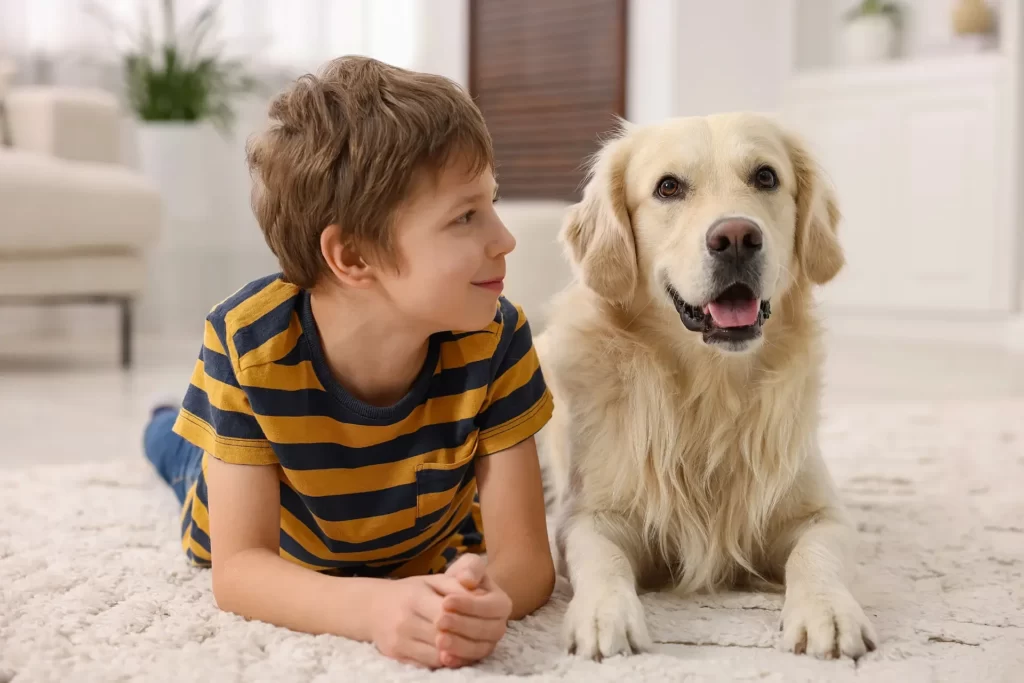 Junge im gestreiften T-Shirt liegt mit einem Golden Retriever auf einem Teppich
