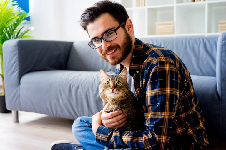 Junge Frau streichelt eine getigerte Katze, die entspannt auf weißer Decke liegt